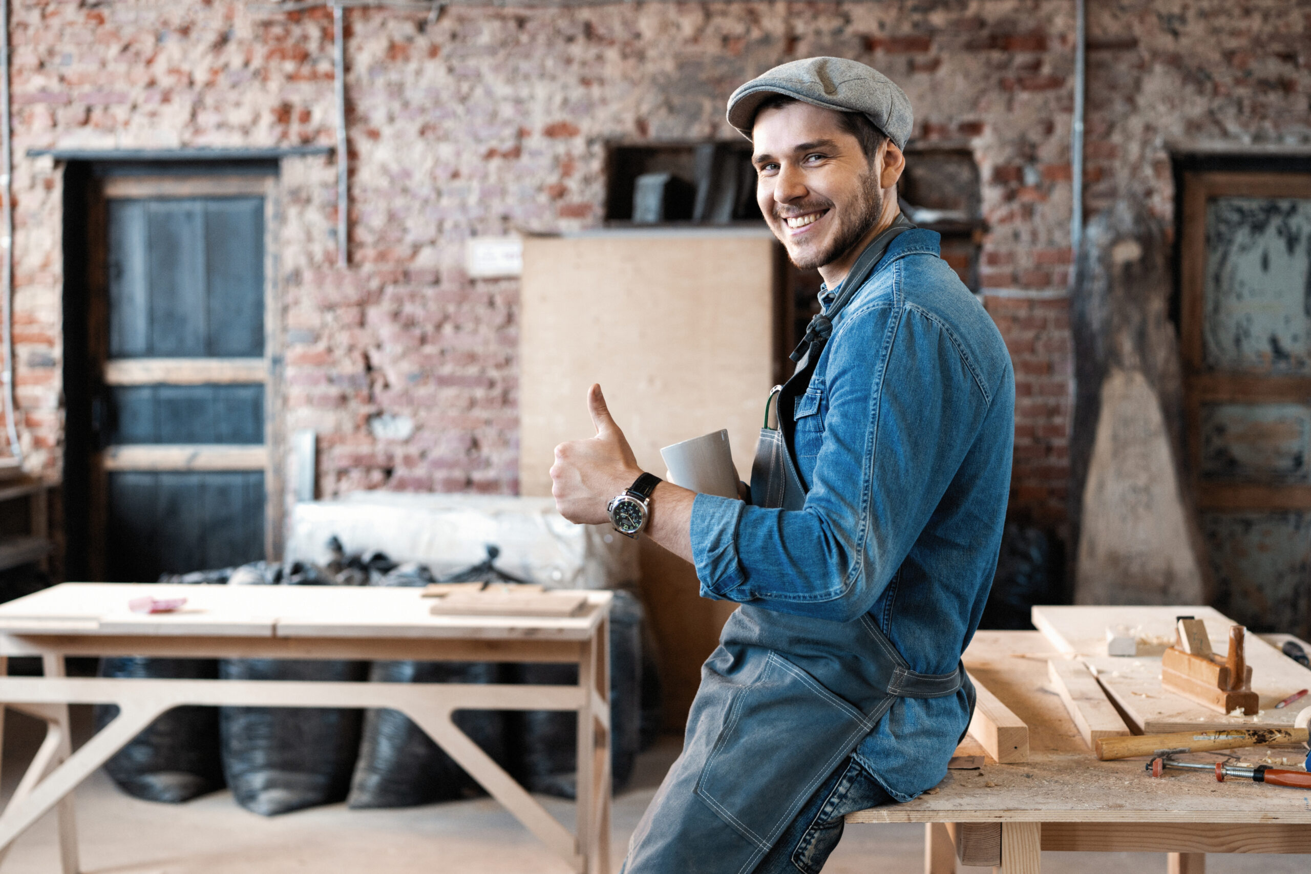 Young joiner work at his workstation. Successful handsome businessman with stylish cap work in carpentry